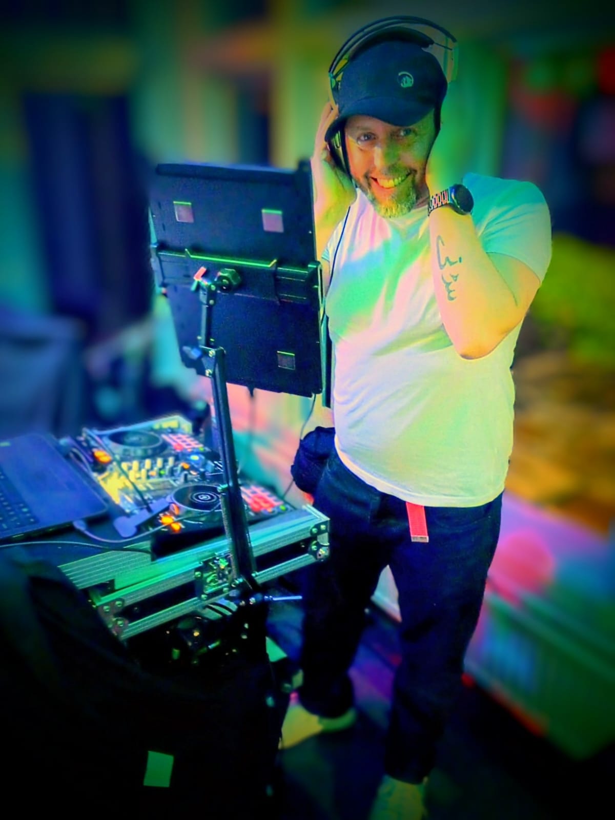 Simon DJ set with headphones smiling at the decks under green and blue lighting